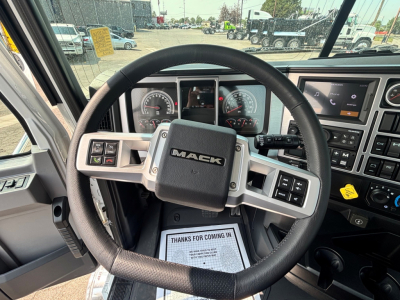Mack PI64T truck interior showing steering wheel with Mack logo, instrument cluster, and center dashboard. Accessories include controls on steering wheel and a screen on the right.