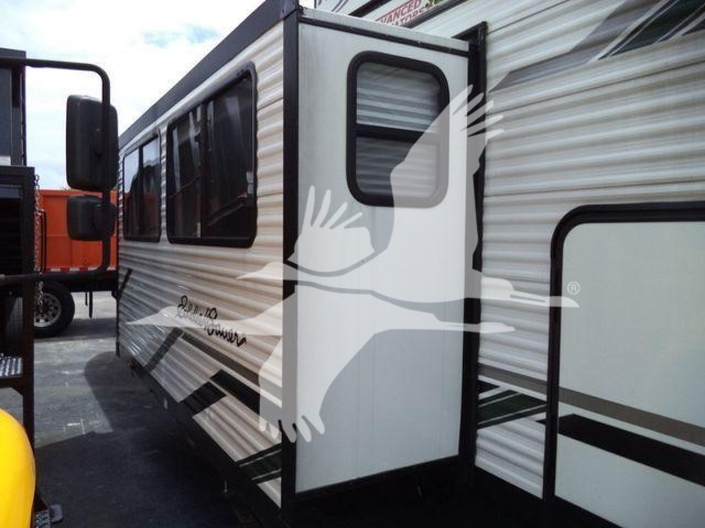 Travel trailer side view with slide-out extended, aluminum siding, window and entry door visible; identification text on side partially legible.