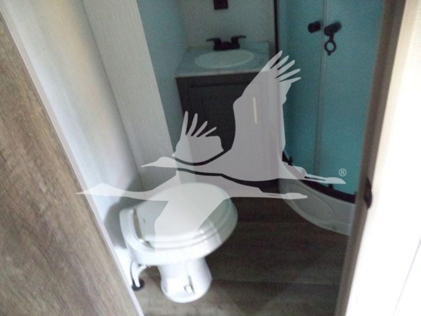 Travel trailer interior photo showing small bathroom with toilet and sink, compact vanity, and shower in background.