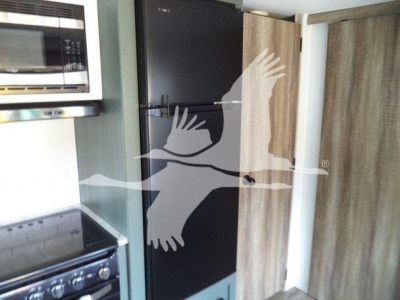 Travel trailer interior showing a black refrigerator, microwave, and adjacent wooden cabinet in a compact kitchen area.