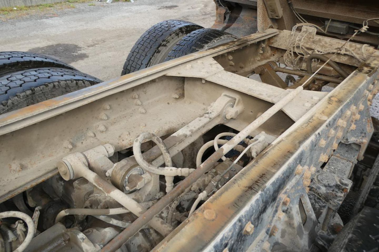 Dump truck chassis showing exposed frame and suspension components with dual rear tires; dirt and grime on metal frame.