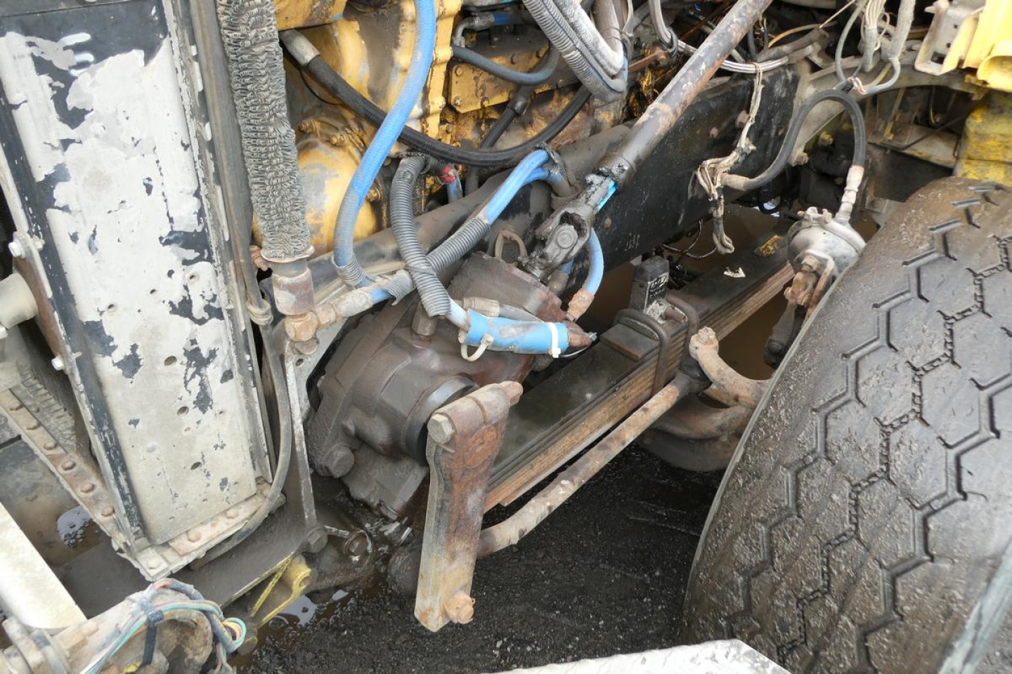 Peterbilt 357 dump truck front suspension with visible hydraulics and blue wiring harness, coolant reservoir, and wheel; engine bay area exposed.