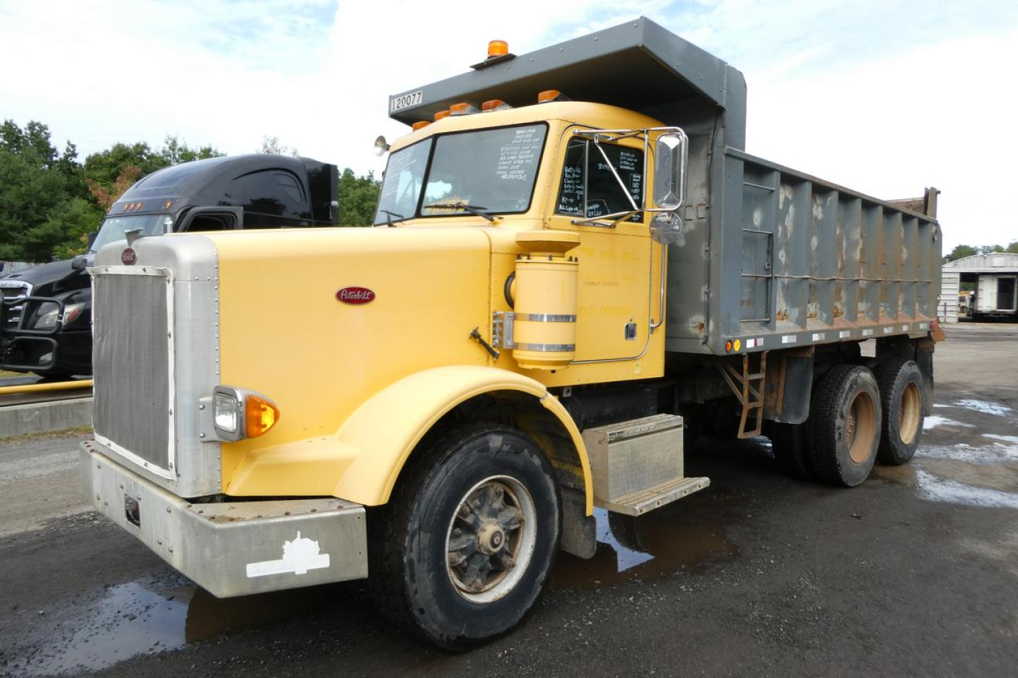 Peterbilt dump truck in use showing cab and dumping dump bed, yellow cab with chrome grille and large front bumper, VIN 1XPALB0X3JN264708 visible on windshield area.