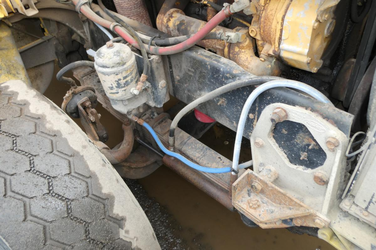 Peterbilt truck engine bay showing hydraulic tank, hoses, and chassis components near front wheel.