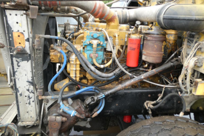 Tractor-engine bay of a 1988 Peterbilt 357 dump truck showing diesel engine with blue pump, red filter, hoses, and metallic components.