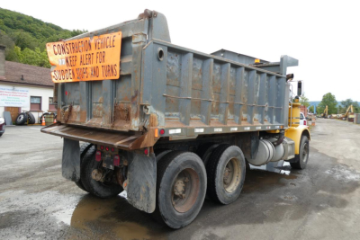 Dump truck rear and left side showing rusty bed with construction vehicle sign and multiple axles.