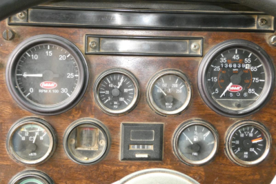 Dashboard of a 1988 Peterbilt 357 showing multiple gauges including tachometer, pressure gauges, coolant temp, and speedometer on a wooden panel.