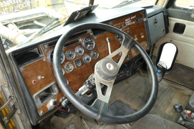Peterbilt truck cabin dashboard with wooden panel, steering wheel, multiple gauges, and gear shifter visible.