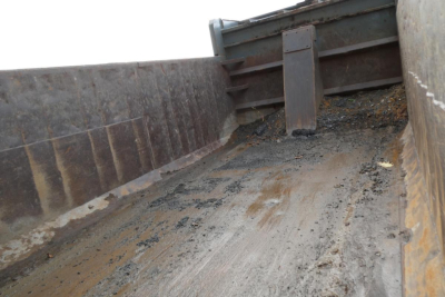 Dump truck bed interior showing dirt, grime, and side walls with a metal bulkhead and scraped floor surface.