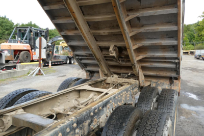 Peterbilt dump truck chassis and raised dump bed showing dual rear axles and undercarriage with hydraulic linkage and rust-resistance soiled components