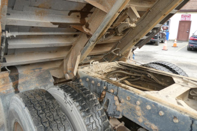 Peterbilt 357 dump truck chassis and dump bed rear wheel area with hydraulic components and rusted steel frame.