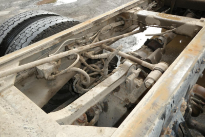 Peterbilt truck chassis view showing exposed frame, suspension, and hydraulic lines in a dump truck. Mechanical components and wiring visible.