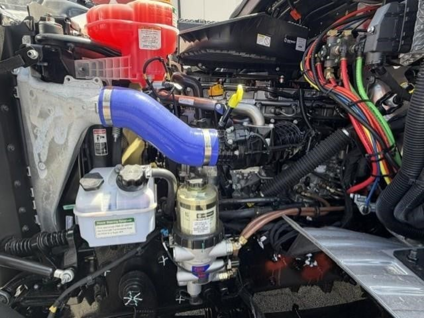 Engine bay of a Western Star 47X dump truck showing blue silicone hose, coolant reservoir, fuel filter, wiring harness, and turbine-style intake components.