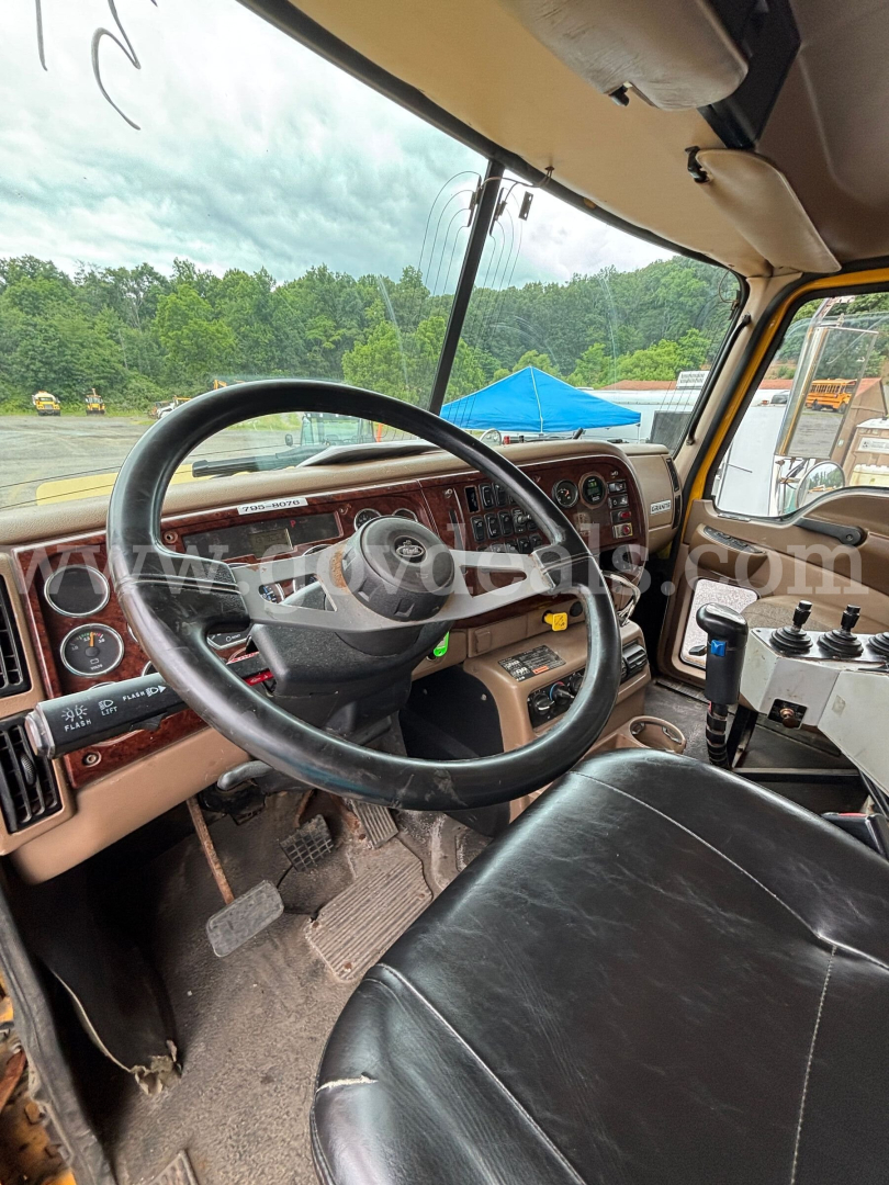 Cab view of 2006 Mack CV713 dump truck showing steering wheel, dashboard with wood trim, accelerator/brake pedals, and gear shifter.