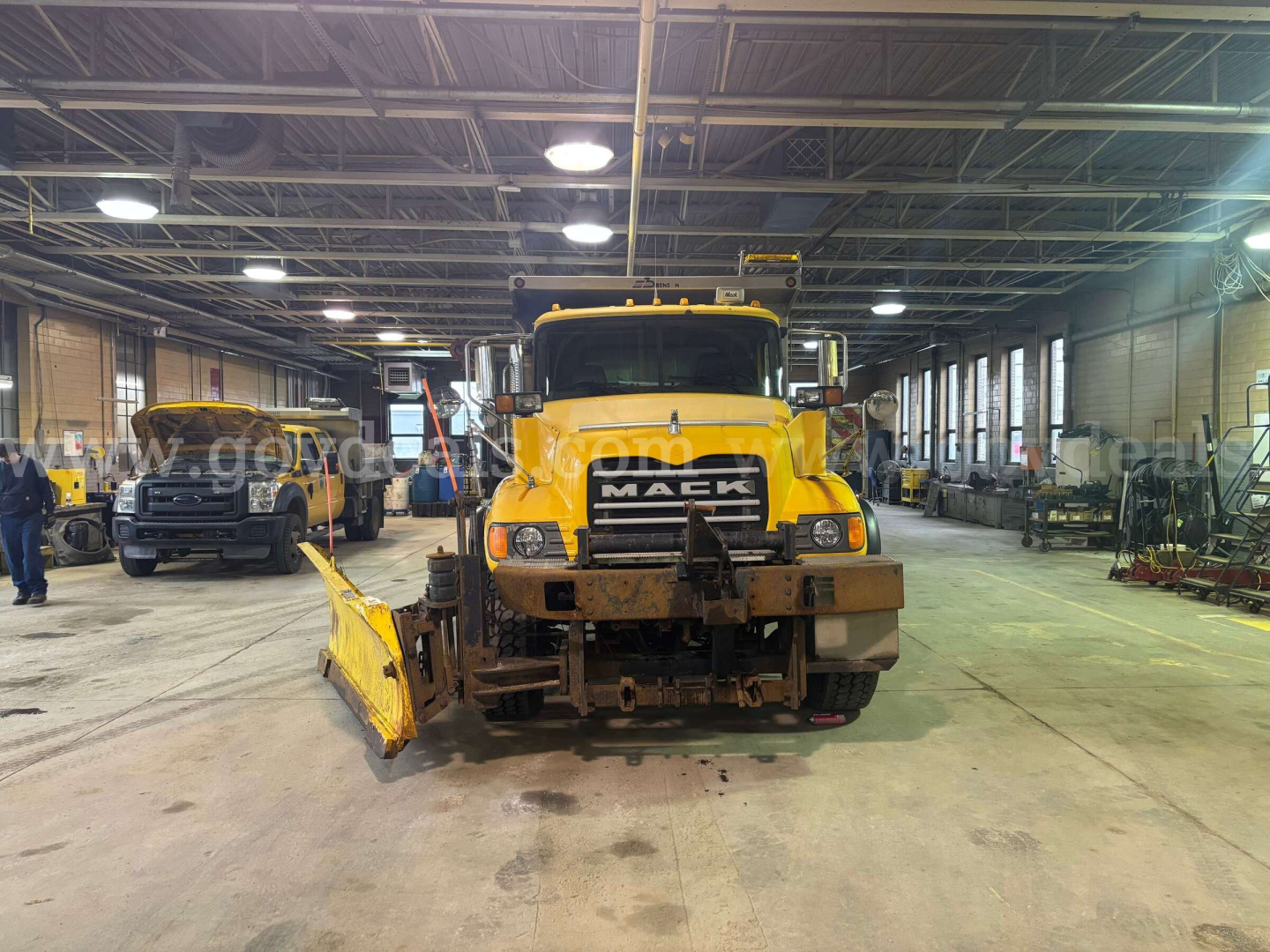 Mack CV713 dump truck front view in a shop with snow plow attachment and visible grille