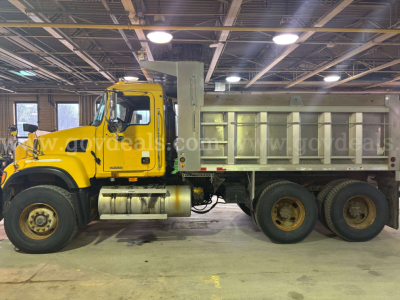 Truck side view showing yellow Mack CV713 dump truck with silver dump bed in an indoor facility.