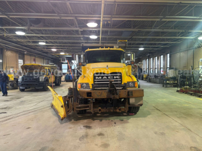 Mack CV713 dump truck front view in a shop with snow plow attachment and visible grille