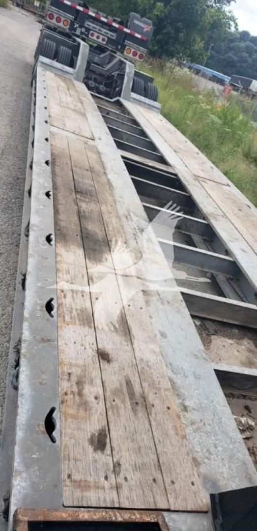 Trailer deck on a lowboy trailer showing wooden planks and steel frame with wheel wells and hitch area visible at the front.