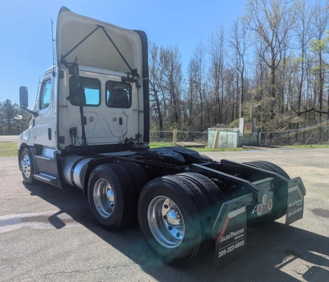 Freightliner Cascadia 126 day cab tractor rear/side view showing dual rear axles and fifth wheel, white cab, chrome wheels and black mud flaps