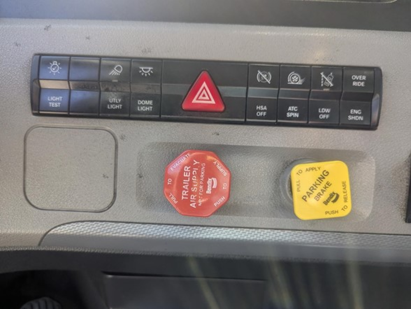 Dashboard panel of a Freightliner Cascadia showing control buttons and two colored knobs (red and yellow) with warning texts.