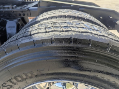 Front wheel and tire of a Freightliner Cascadia 126 day cab, centered dual tire with tread visible; part of chassis and suspension in the background.