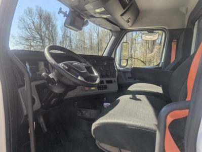 Freightliner Cascadia interior cabin view showing steering wheel and dashboard with driver seat and orange accents.