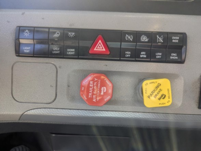 Dashboard panel of a Freightliner Cascadia showing control buttons and two colored knobs (red and yellow) with warning texts.
