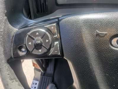 Truck steering wheel controls in a Freightliner Cascadia cab showing circular navigation pad with OK center button and arrow keys.