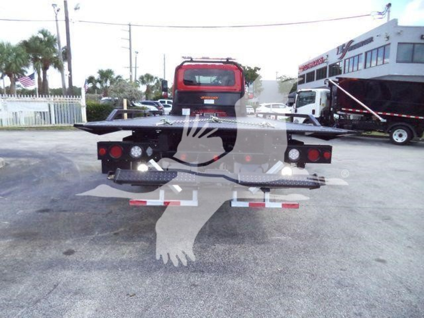 Flatbed rollback truck rear view with red cab and black dual rear lights in a dealership lot.