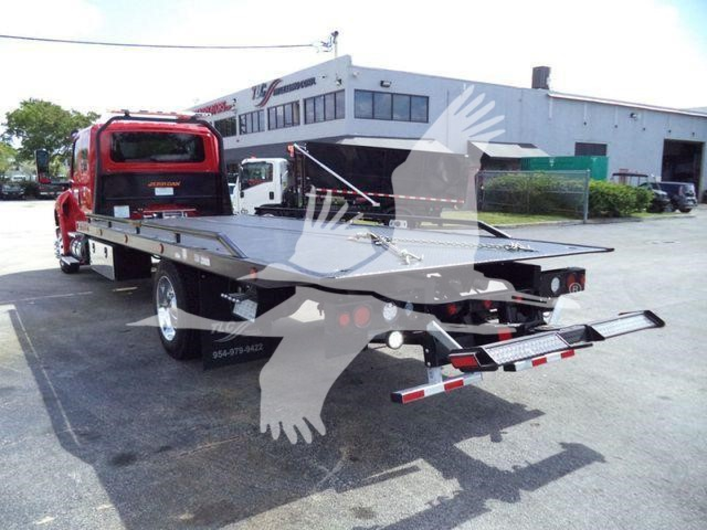 Truck in lot showing a flatbed rollback with red cab and dual rear axles; license plate area and rear equipment visible.