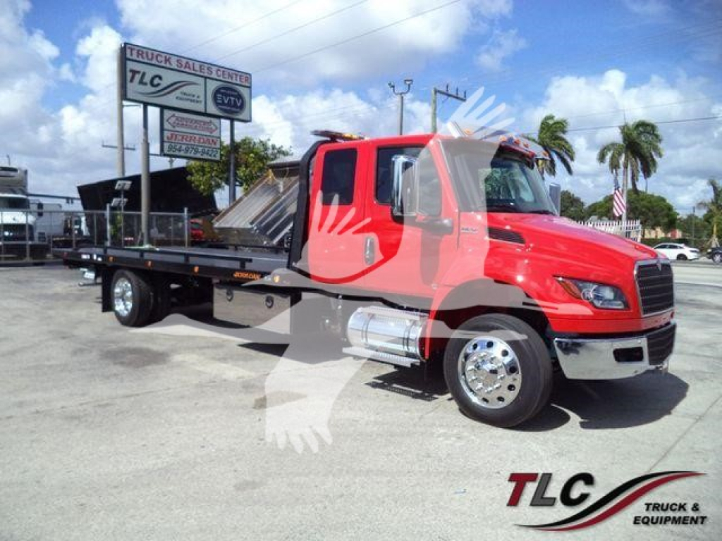 Truck with red cab and flatbed in a dealership lot. Visible text: 7LC Truck Sales Center sign, International-style grille, chrome wheels. Foreground watermark of TLG.