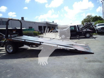 Truck rollback tow truck and flatbed trailer in a dealership lot.