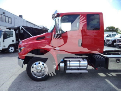 Truck cab side view showing red International MV heavy-duty truck with chrome fuel tanks and steps, rolling stock in background.