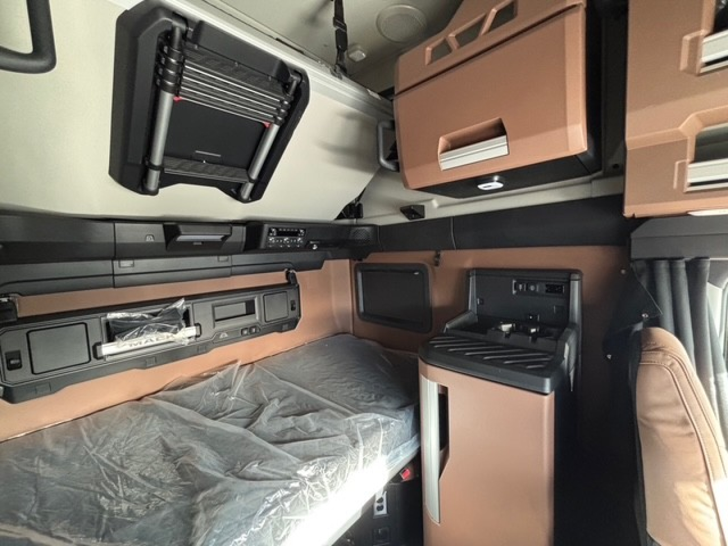 Mack PR64T76H cab interior showing sleeper area with overhead compartments, storage bins, and a small fridge cabinet.