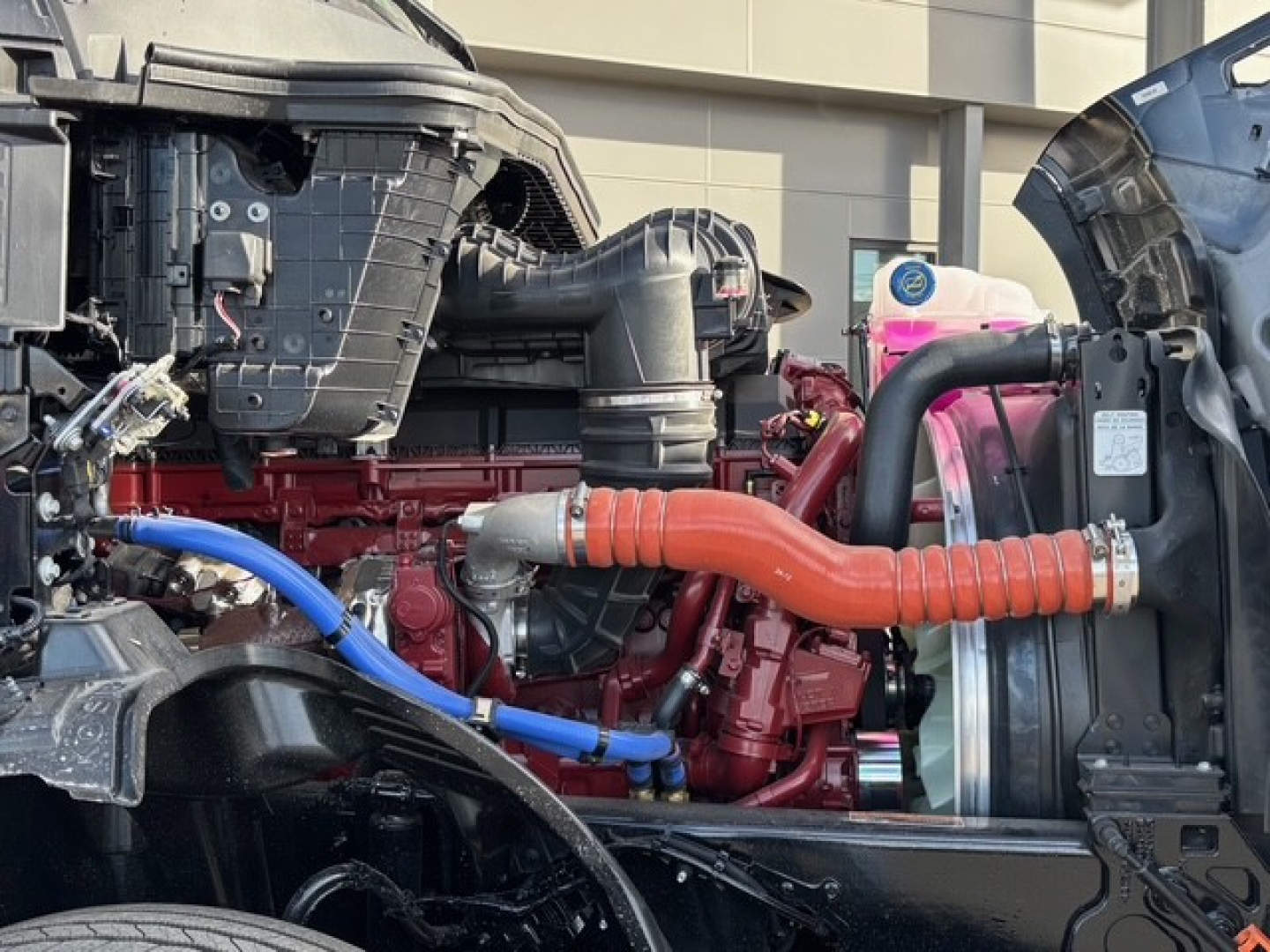 Truck engine bay with red diesel engine, orange coolant hose, blue hose, radiator and surrounding components visible.