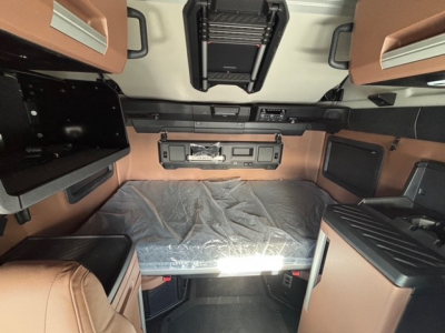 Truck cab interior showing sleeper bed with overhead storage and controls, Mack PR64T76H cabin layout.