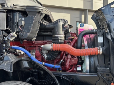 Truck engine bay with red diesel engine, orange coolant hose, blue hose, radiator and surrounding components visible.