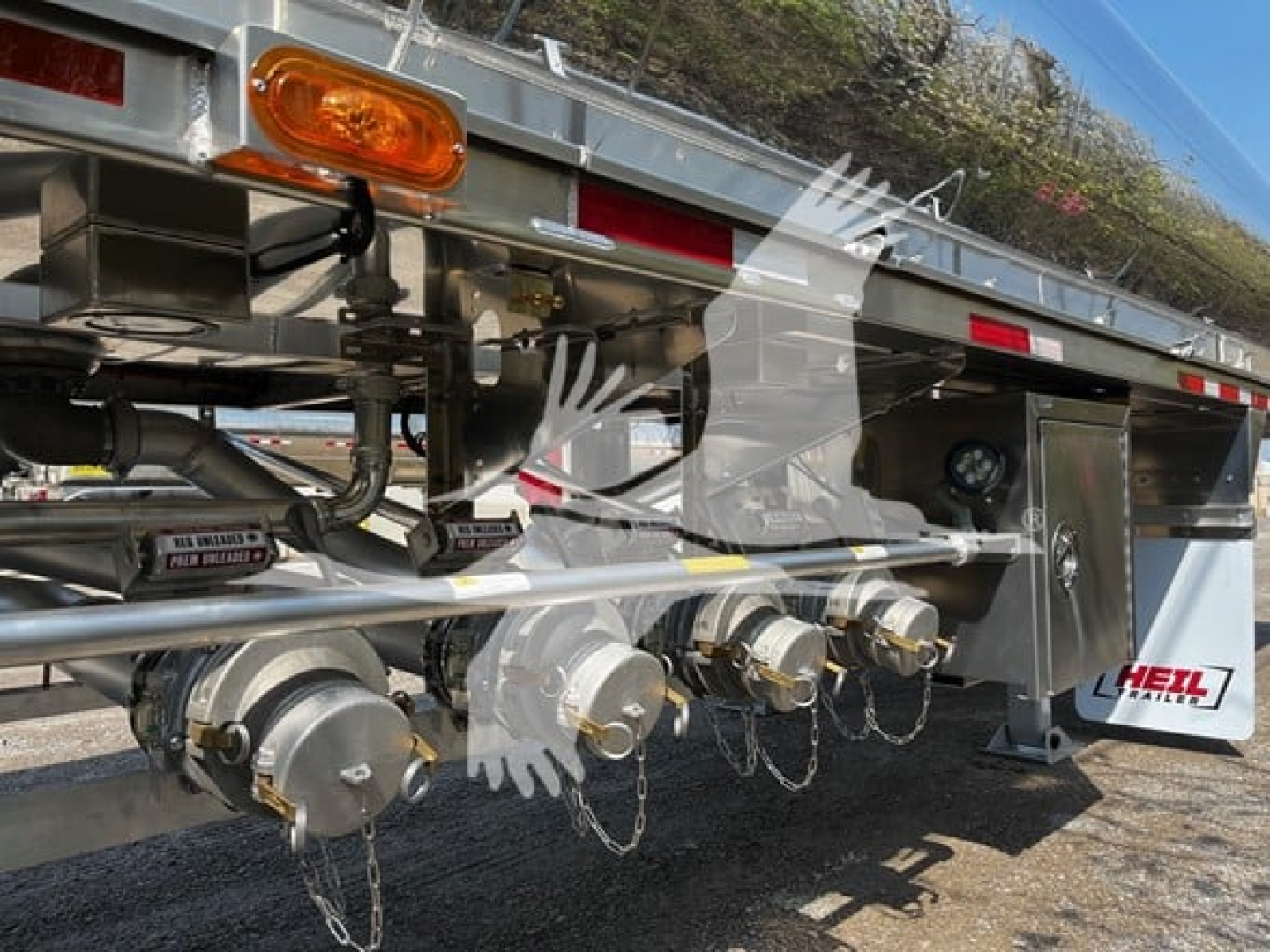 Trailer underside showing multiple hose couplers and valves, heavy-duty chrome fittings, safety chains, and a boxed control box on a Heil 4-comp trailer.