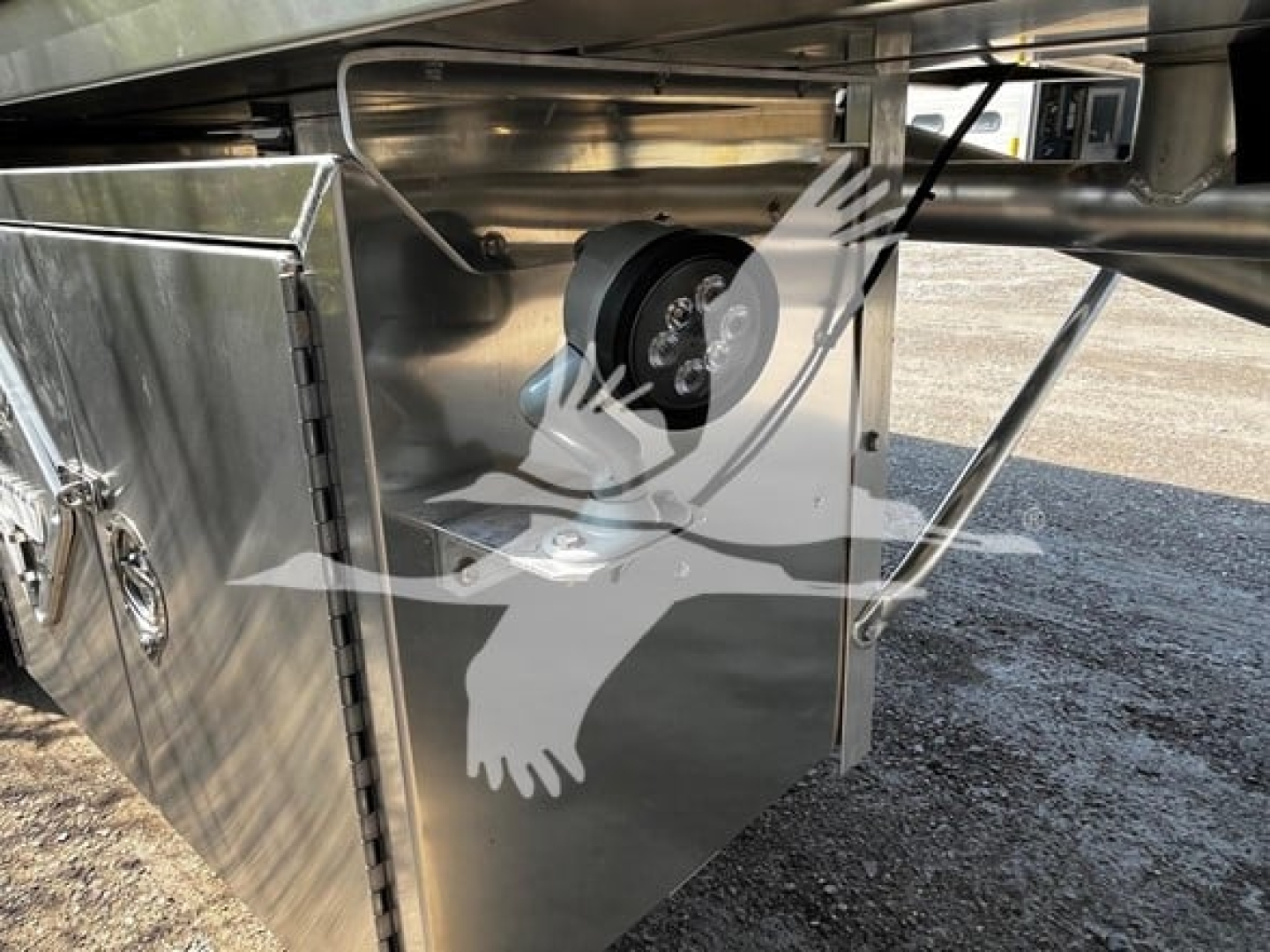 Trailer undercarriage showing a round wheel or reel mounted inside a polished stainless steel box with a latch panel, part of a Heil 4-Comp trailer