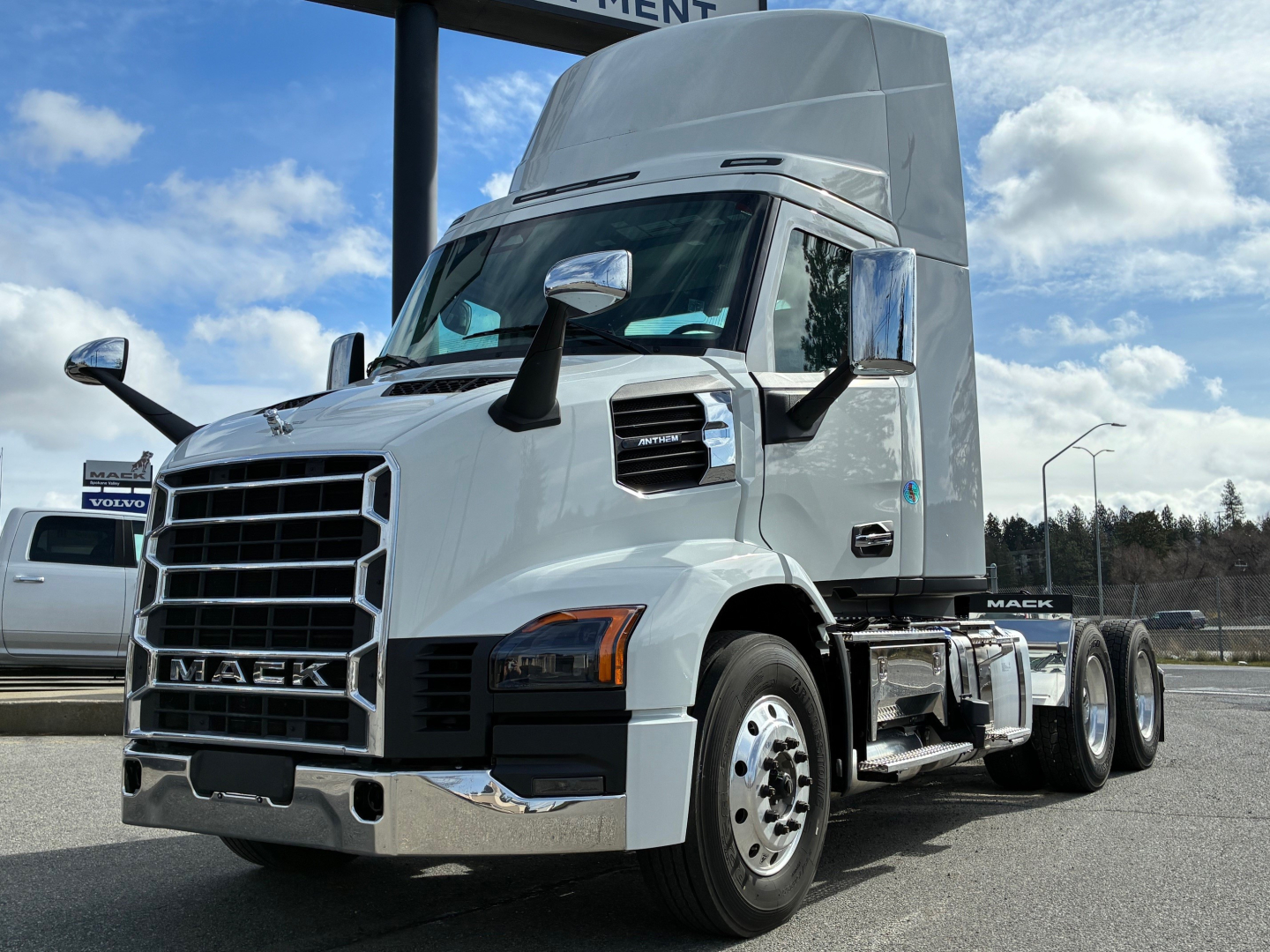 Mack AN64T conventional daycab truck front-left view showing chrome grille, Mack emblem, large side mirrors, and elevated sleeper cab.