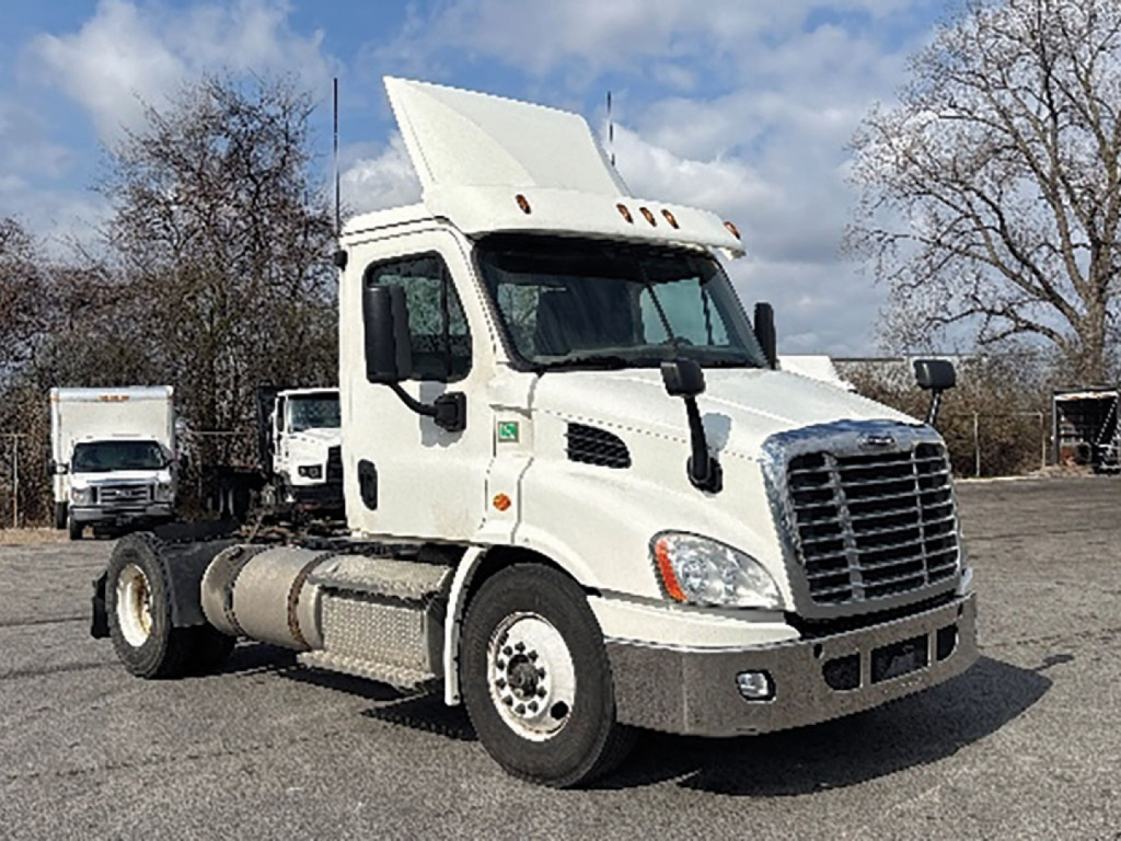 Truck cab in view showing Freightliner Cascadia Daycab with raised sleeper, front grille, and fuel tanks on the side.