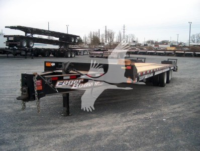 Trailer showing Eager Beaver logo on black front with dual tandem axle and long flatbed, in a yard with other trailers.