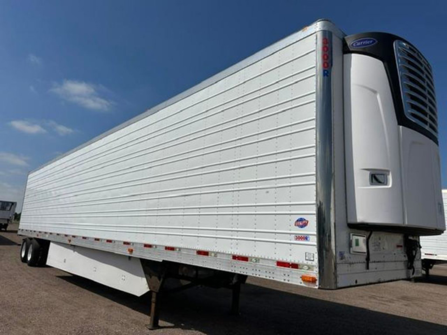Trailer refrigeration unit and side of a white 2016 utility reefer trailer with vertical paneling and a Carrier cooling unit at the front right.