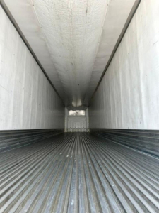 Trailer interior view showing ribbed floor and white side walls of a refrigerated trailer.