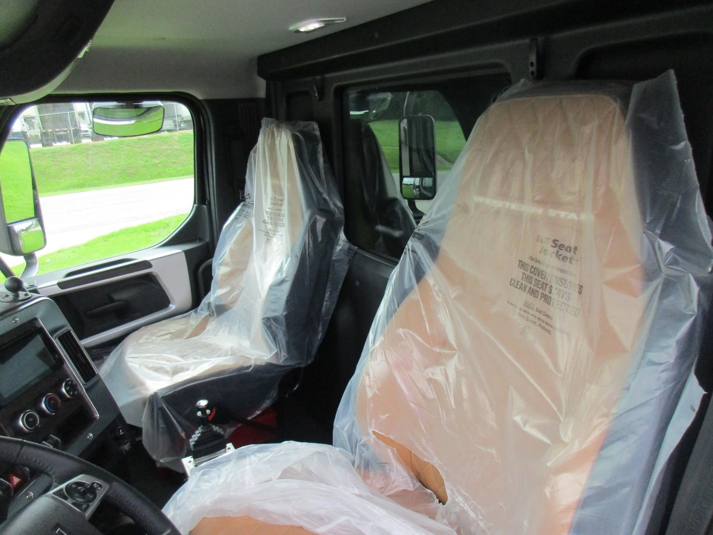 Truck cabin interior of a new Western Star 49X with plastic seat covers; driver and passenger seats visible with protection sheet.
