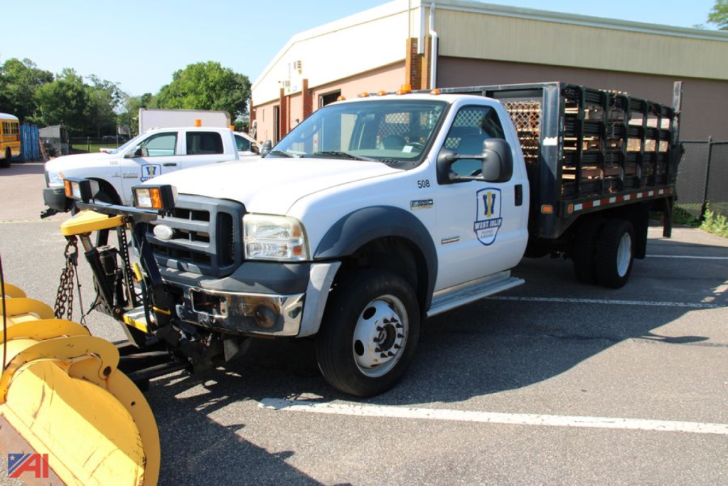 2006 Ford F550 Super Duty rack truck with plow and stake bed, front-left view.