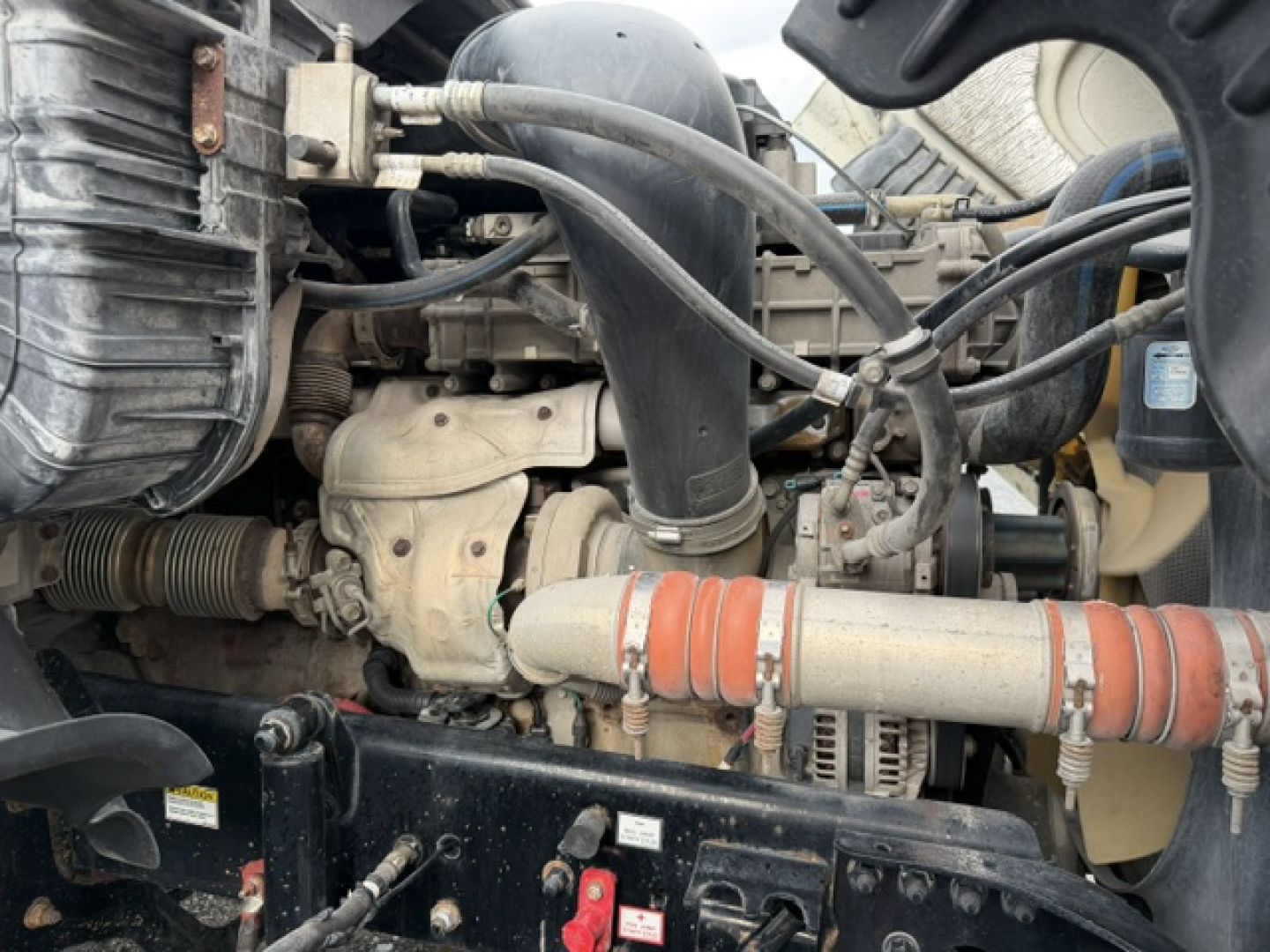 Engine bay of a Freightliner Cascadia showing turbocharger, hoses, radiator, and orange coolant hose and various metal brackets.