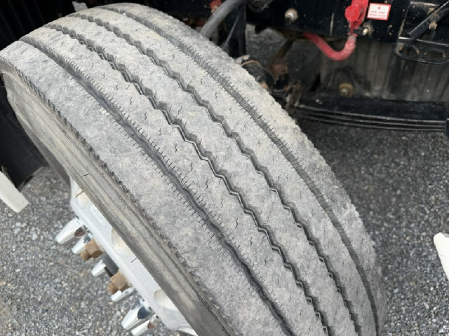 Freightliner Cascadia front tire and wheel with visible tread, part of cab chassis; surrounding components and road grime.