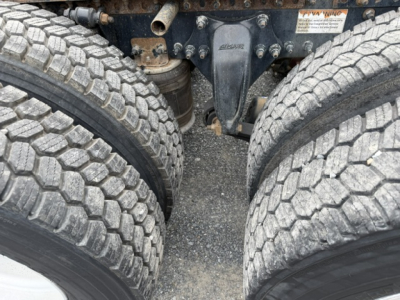 Rear view of Freightliner Cascadia chassis showing dual rear axles and suspension components; visible label with warning text on frame nearby.