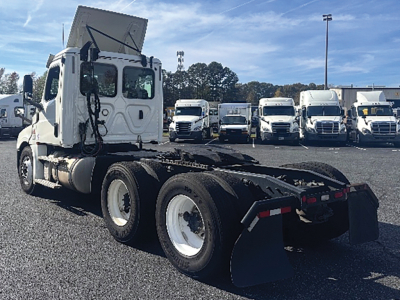 Truck chassis with tractor cab from a Freightliner Cascadia daycab, rear dual-axle with mud flaps and flatbed towing gear visible in lot